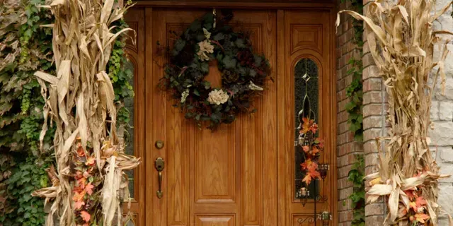 Wooden front door decorated with autumn wreath and harvest garlands on a rustic porch