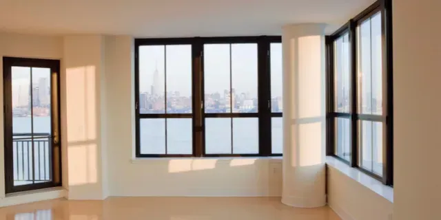 Empty bright room with large windows and a balcony door overlooking a cityscape