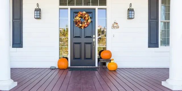 Front porch with a black door, autumn wreath, pumpkins, and white columns on a gray house