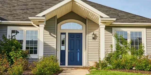 Front exterior of a beige house with a blue front door, white trim, and landscaped shrubs.