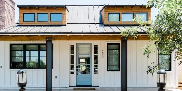 Modern white house facade with blue door, black trim, and two dormer windows