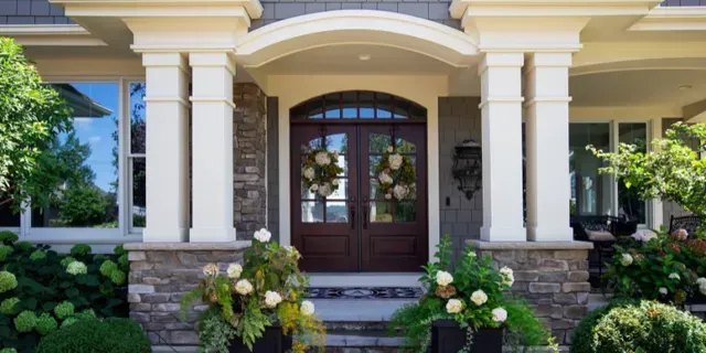 Elegant front porch with stone columns, dark wood double doors, and flower arrangements by the steps
