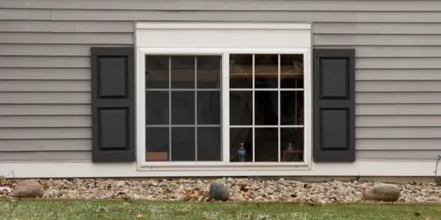 House exterior with gray siding and a white-framed window flanked by black shutters.