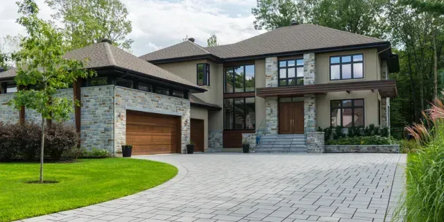 Modern two-story house with stone accents, wood garage, and a wide paved driveway