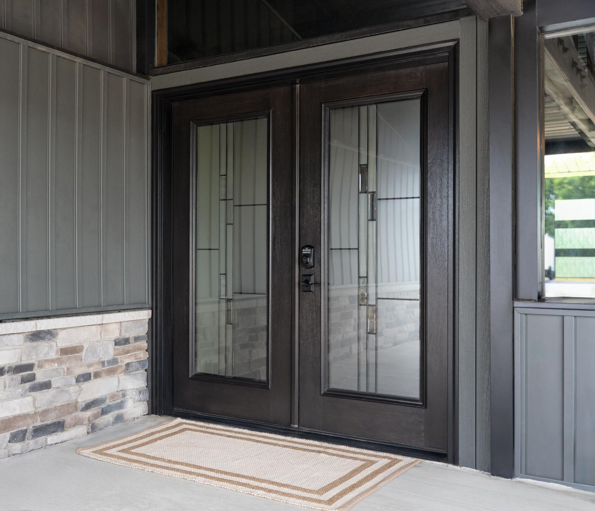 Black double front door with glass panels and a patterned doormat on a covered porch