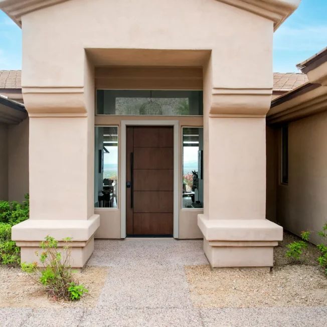 Front entrance of a beige stucco house with a wooden door and small side windows