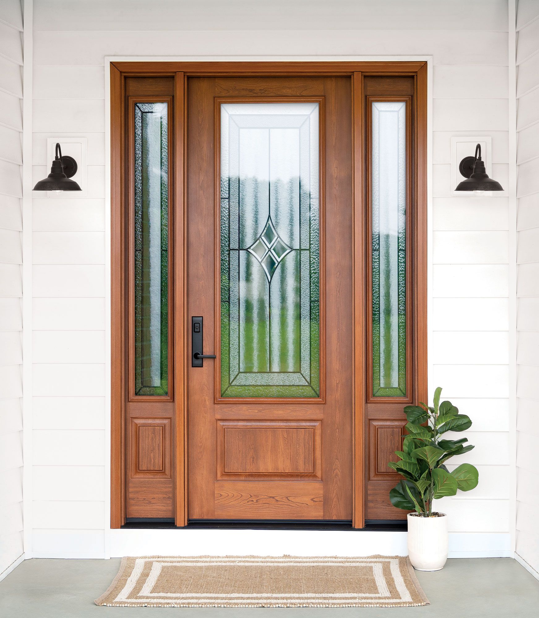 Wooden front door with frosted glass panels, flanked by wall lanterns and a potted plant on the porch.