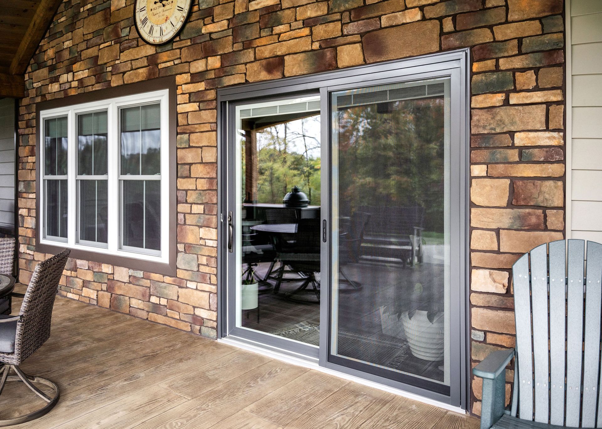 Stone patio with brick house wall, white-trimmed windows, and sliding glass doors leading to a deck.