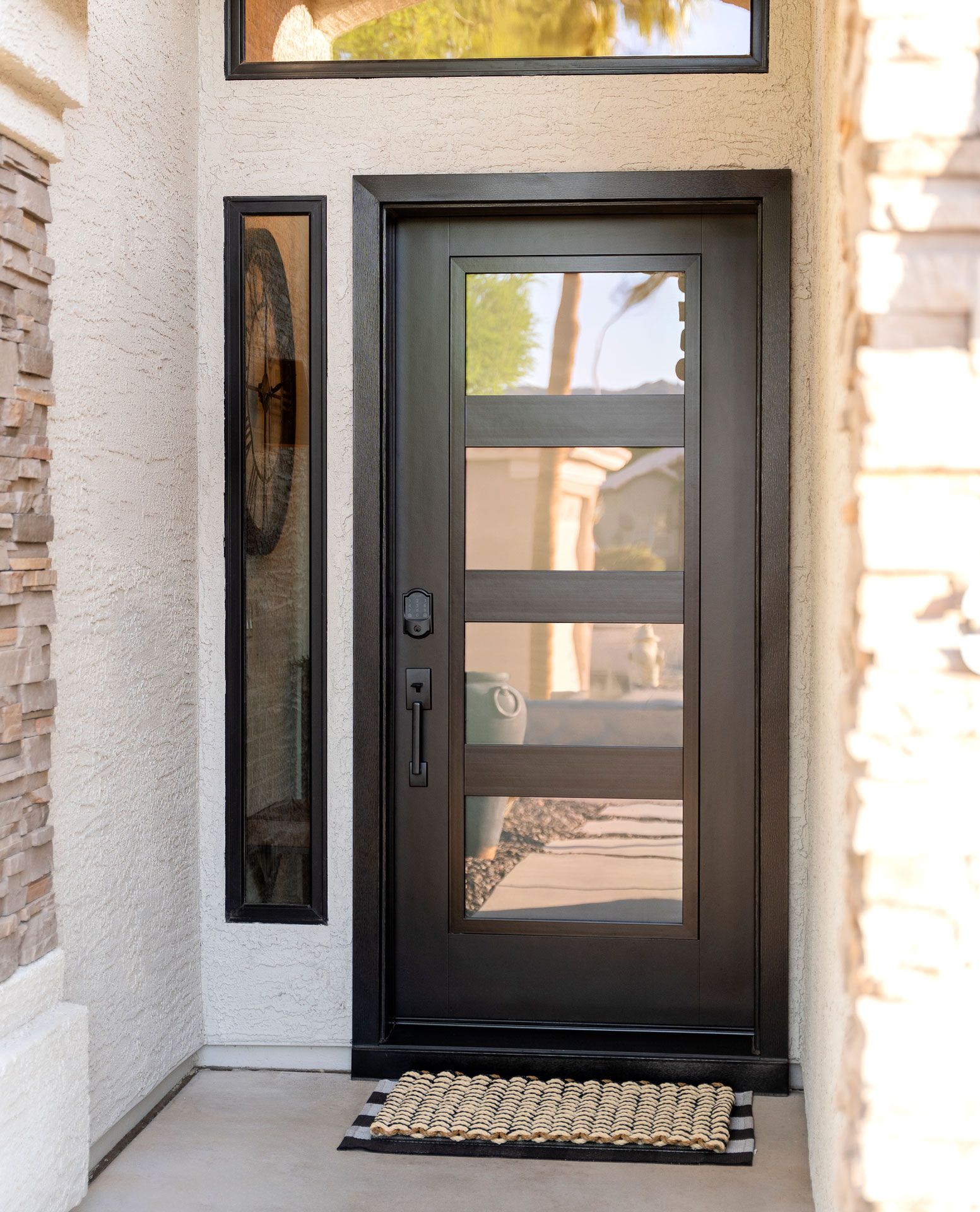 Modern black front door with frosted glass panels and narrow side window beside stone entryway.