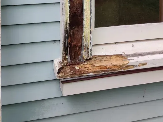 Damaged wooden window frame with peeling paint and rotted trim on a blue house siding