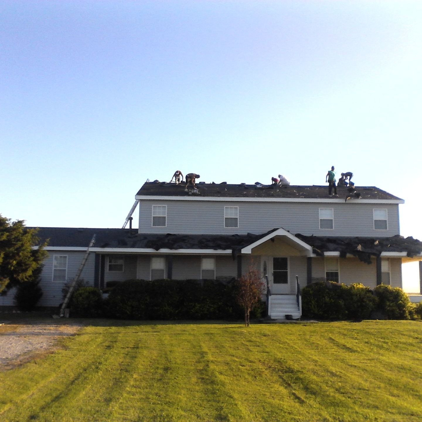 Roofers working on a two-story gray house under a clear blue sky. El Reno, OK