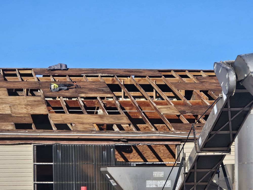 Roof partially torn off a building under construction, worker on site.