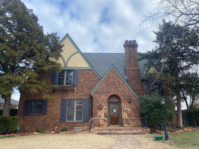 Brick house with slate roof, arched doorway, chimney, and landscaped lawn.