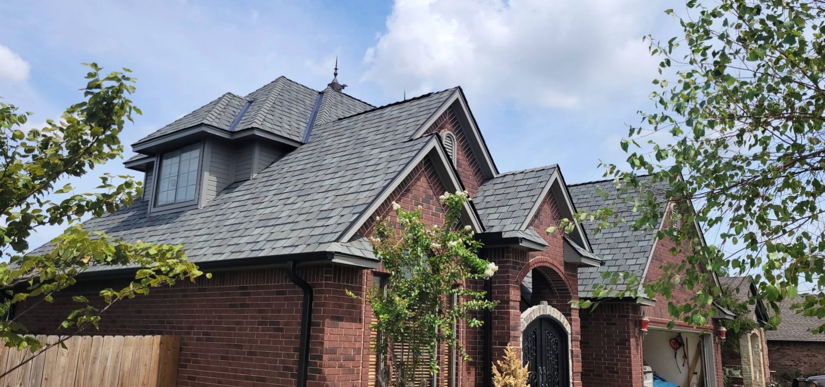 Certainteed Belmont Shingles on Roof and Brick house, windows, and trees in front of a blue sky.