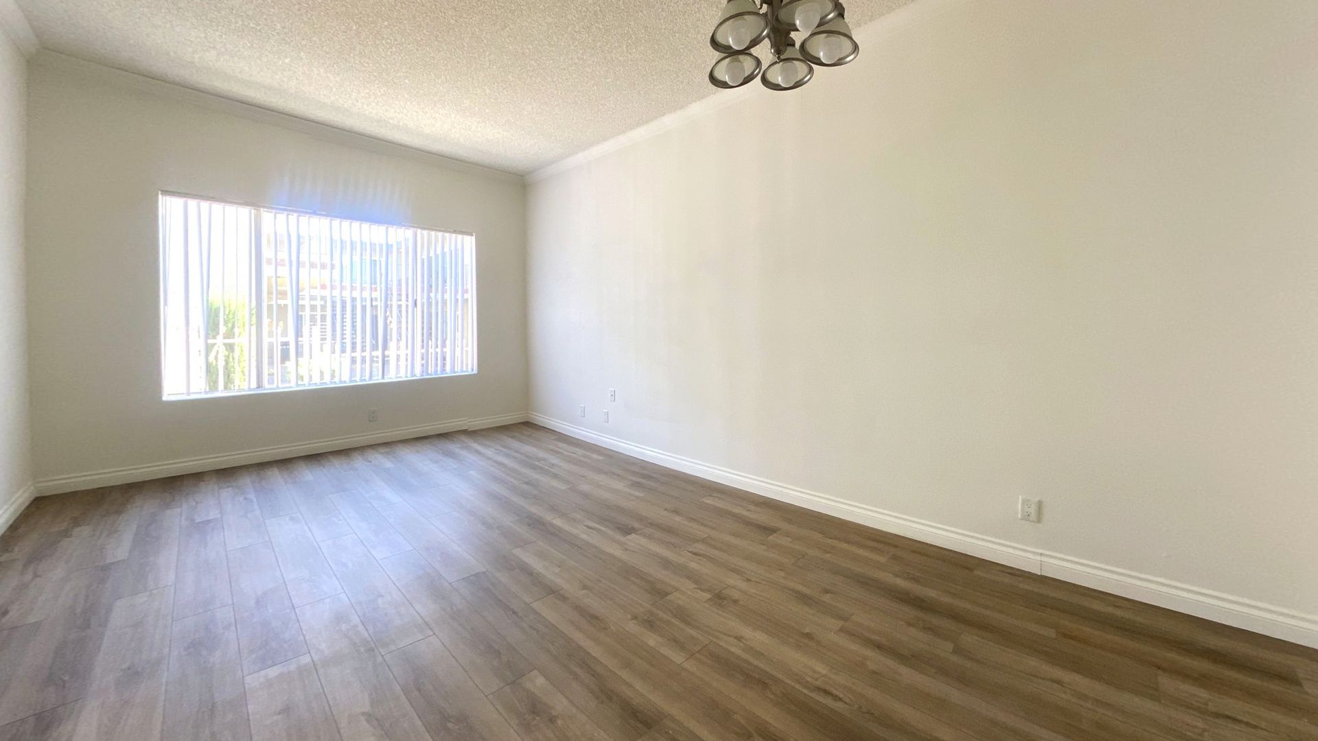 Empty room with wood-look flooring, a window with vertical blinds, and a light fixture.
