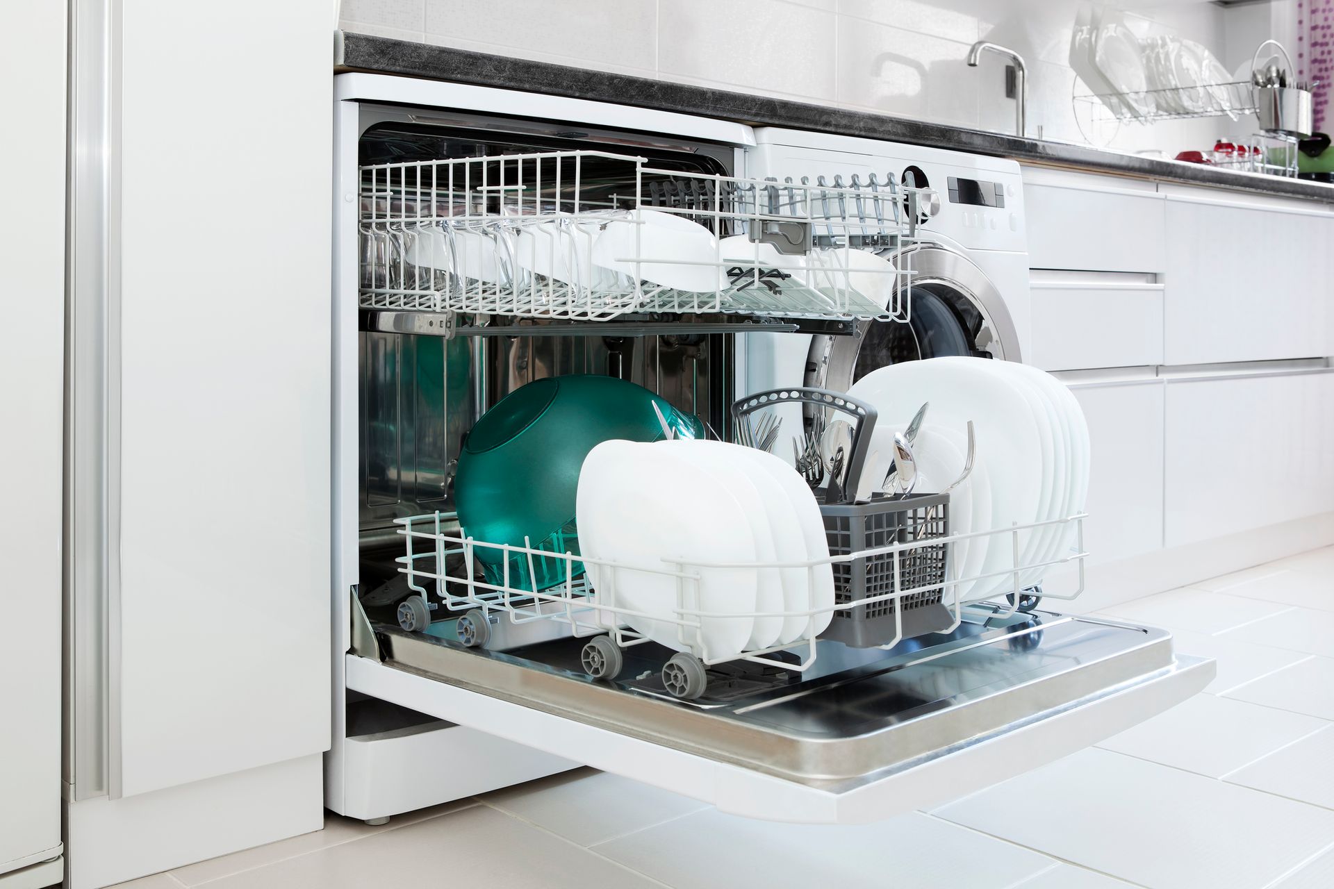 Open dishwasher filled with clean white dishes, bowls, and a green bowl.