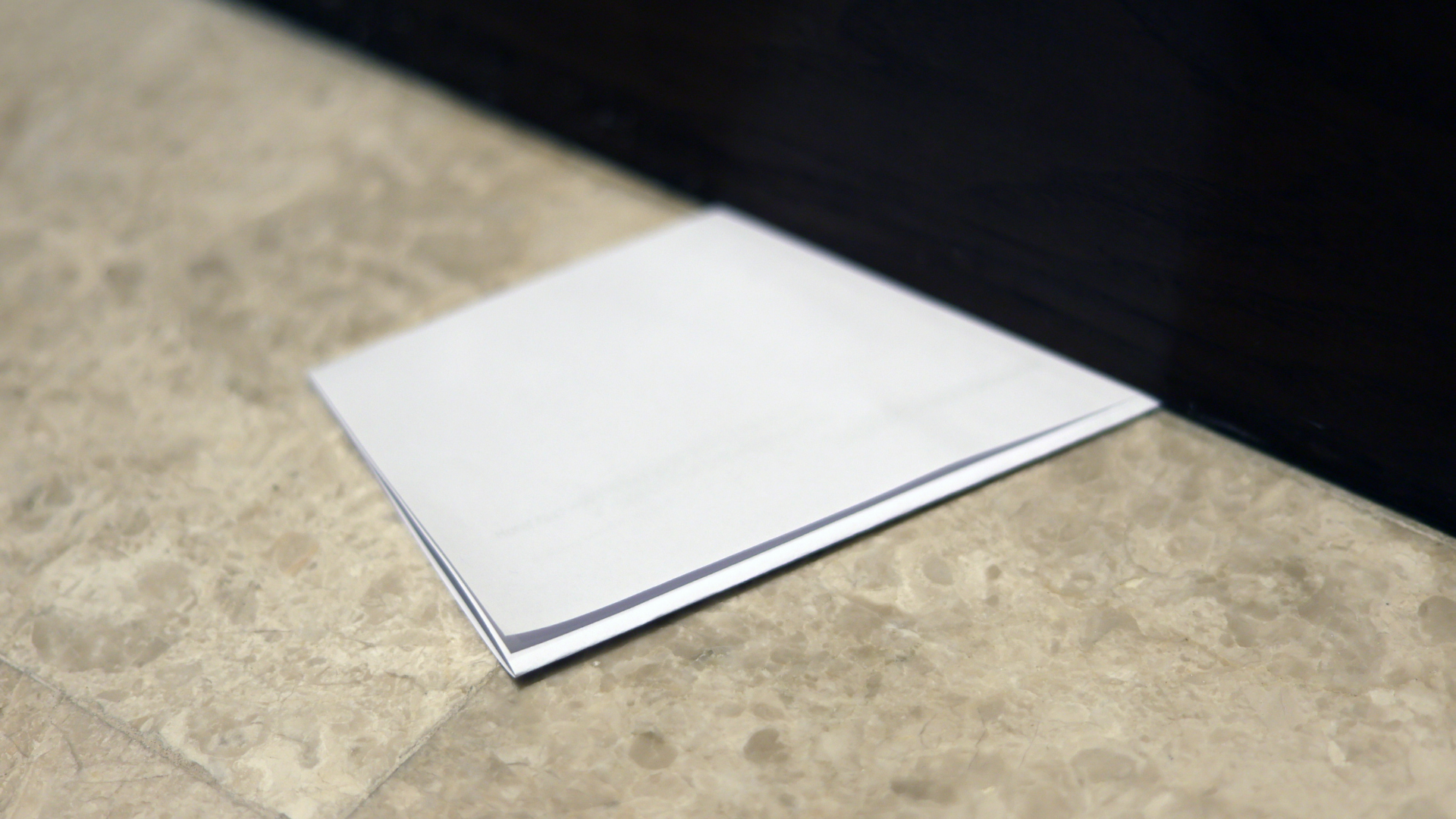 White folded paper on a beige tile floor, next to a black surface.