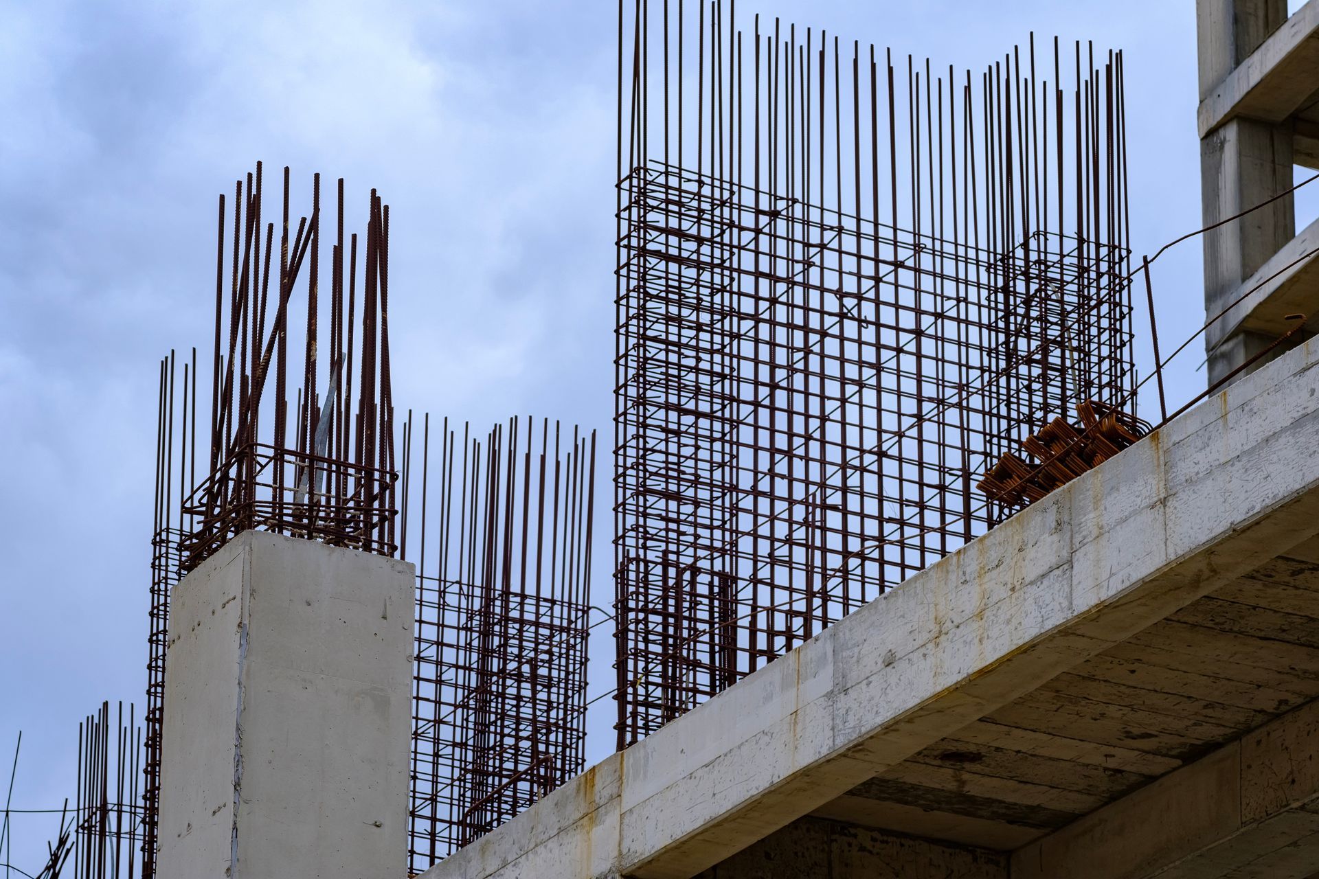Partially built concrete structure with exposed steel rebar against a cloudy sky