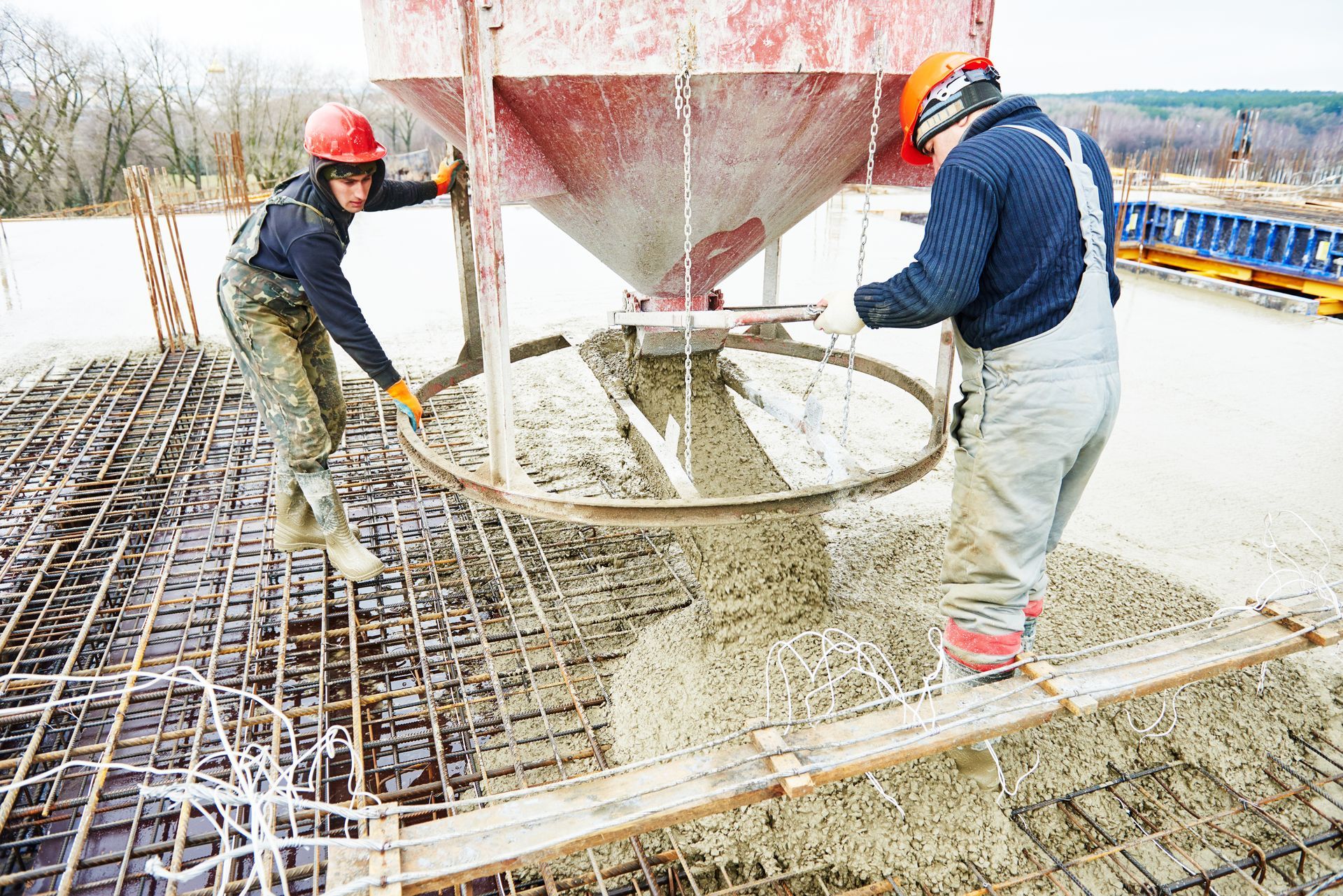 Workers are pouring concrete onto a reinforced steel rebar grid