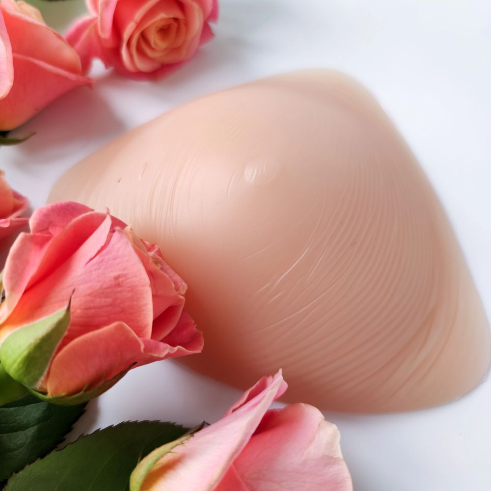 Una protesi mammaria di colore chiaro poggiata su una superficie bianca, circondata da diverse rose rosa tenue.
