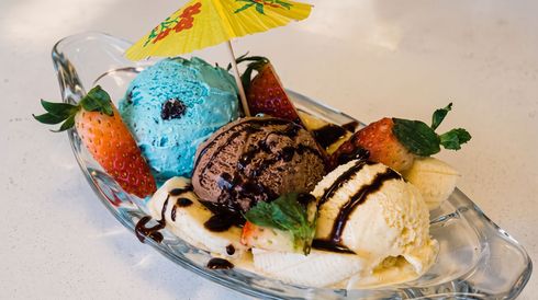 Colorful ice cream sundae in a glass dish, topped with chocolate drizzle, fruit, and a tiny umbrella