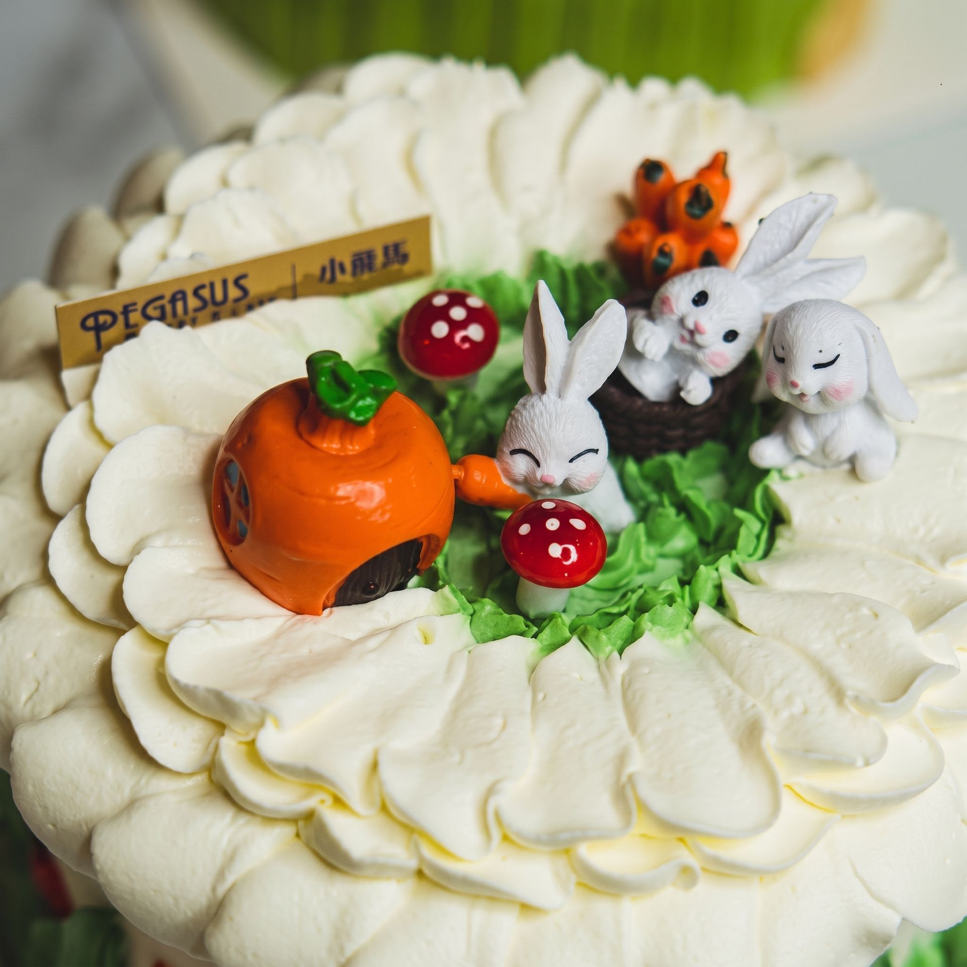 White flower cake topped with carrots, strawberries, and small rabbits in a garden scene