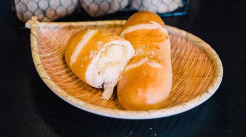 Two golden crusty bread rolls in a woven basket, one split open on a dark table