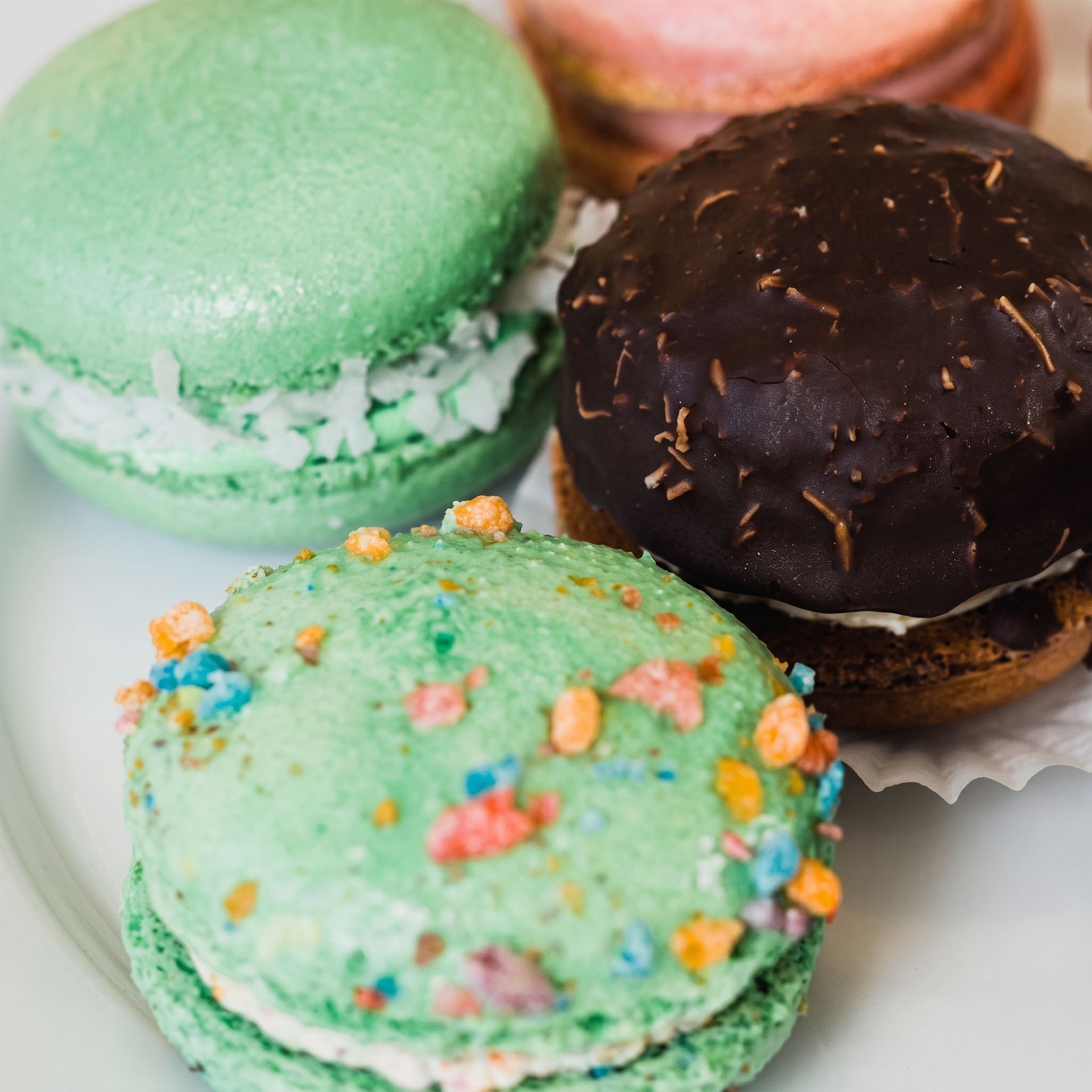 Colorful macarons on a white plate, including green, mint sprinkle-topped, and chocolate varieties.