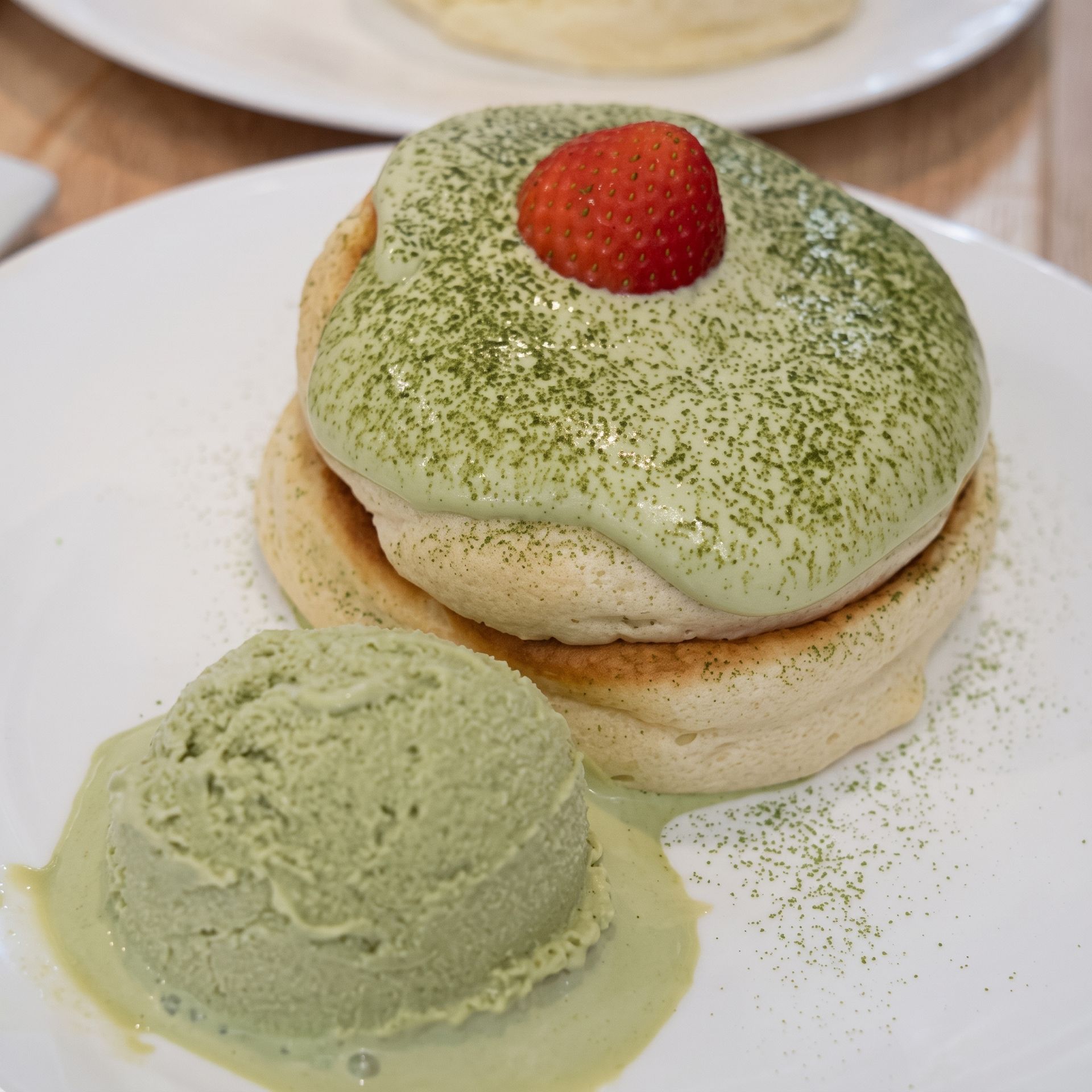 Matcha dessert topped with a strawberry, served with a scoop of green ice cream on a white plate
