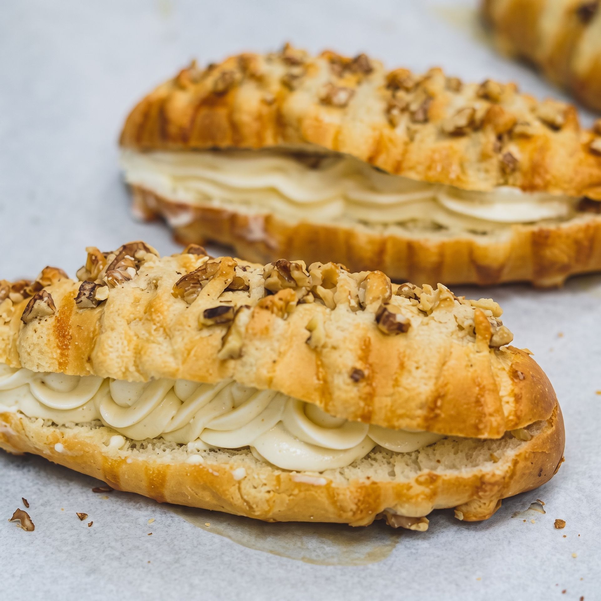 Two cream-filled pastries topped with chopped nuts on a light surface