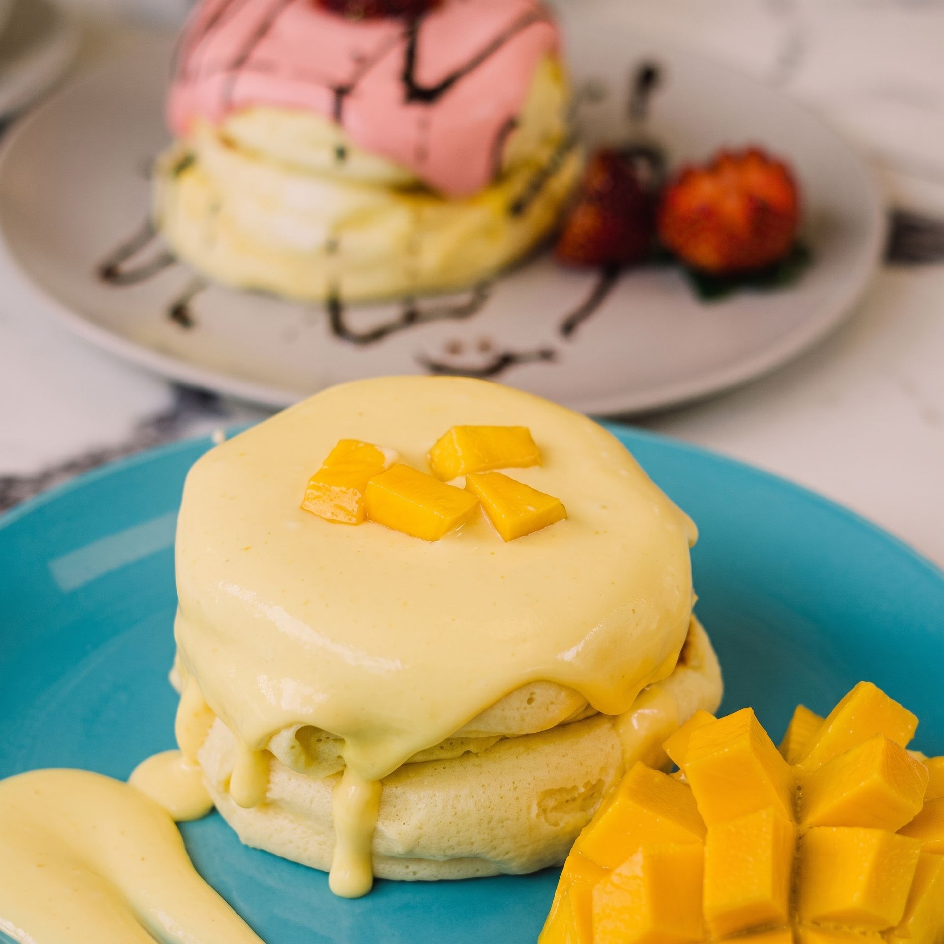Mango-topped pancakes with syrup and diced mango on a blue plate, with more pancakes in the background