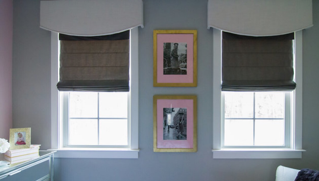A bedroom with two windows and two framed pictures on the wall.