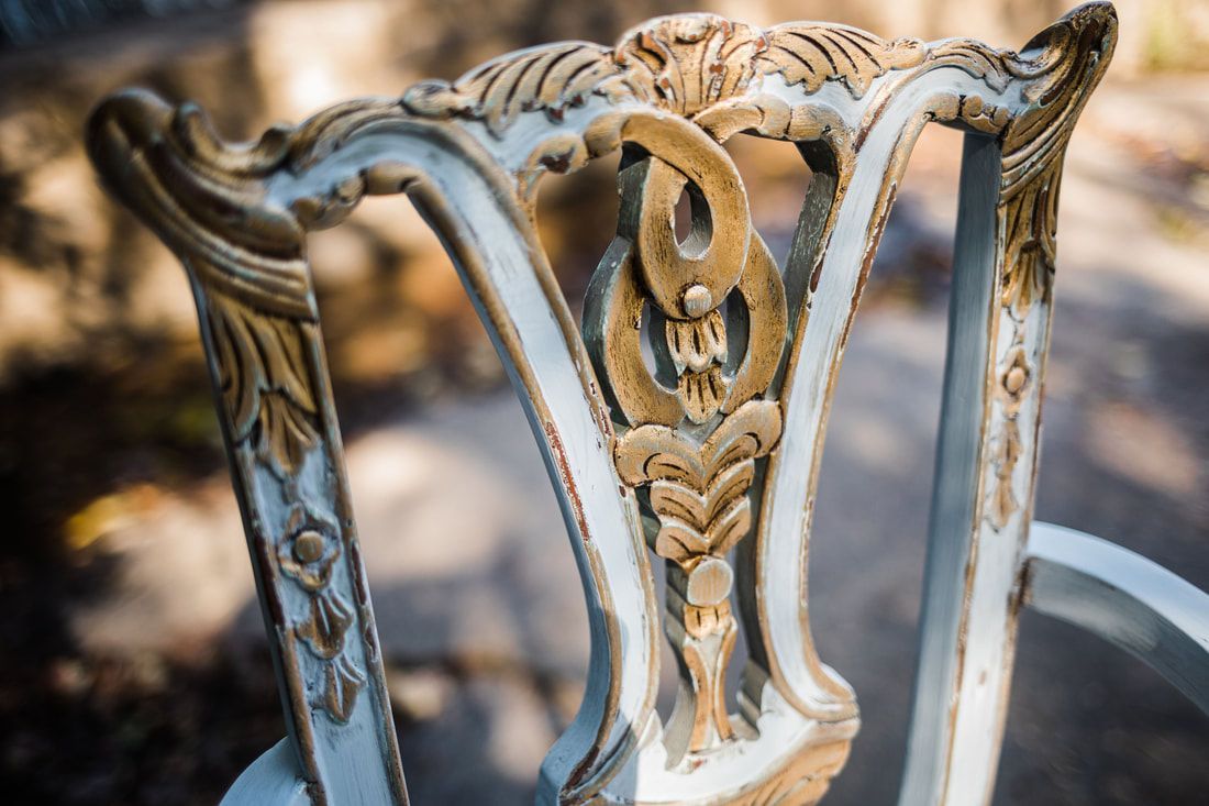 A close up of the back of a white and gold chair.
