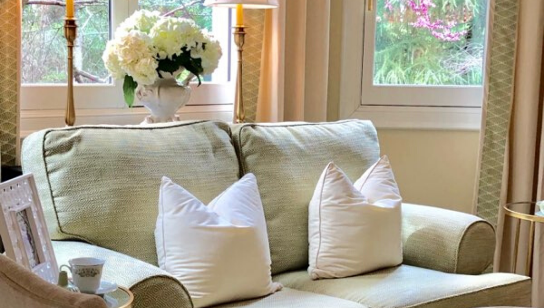 A living room with a couch and chair and a vase of flowers on the window sill.