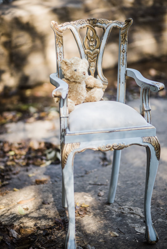 A teddy bear is sitting on a white chair.