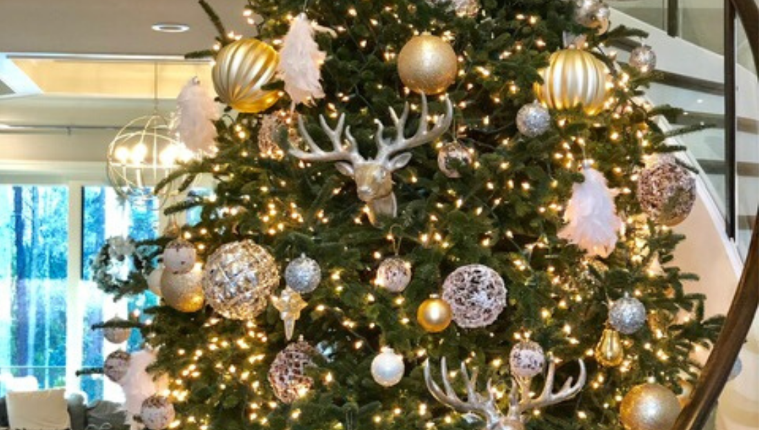 A christmas tree is decorated with gold and silver ornaments and a deer head.