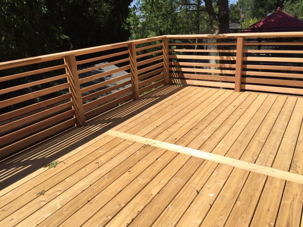 A wooden deck with a wooden railing and trees in the background.