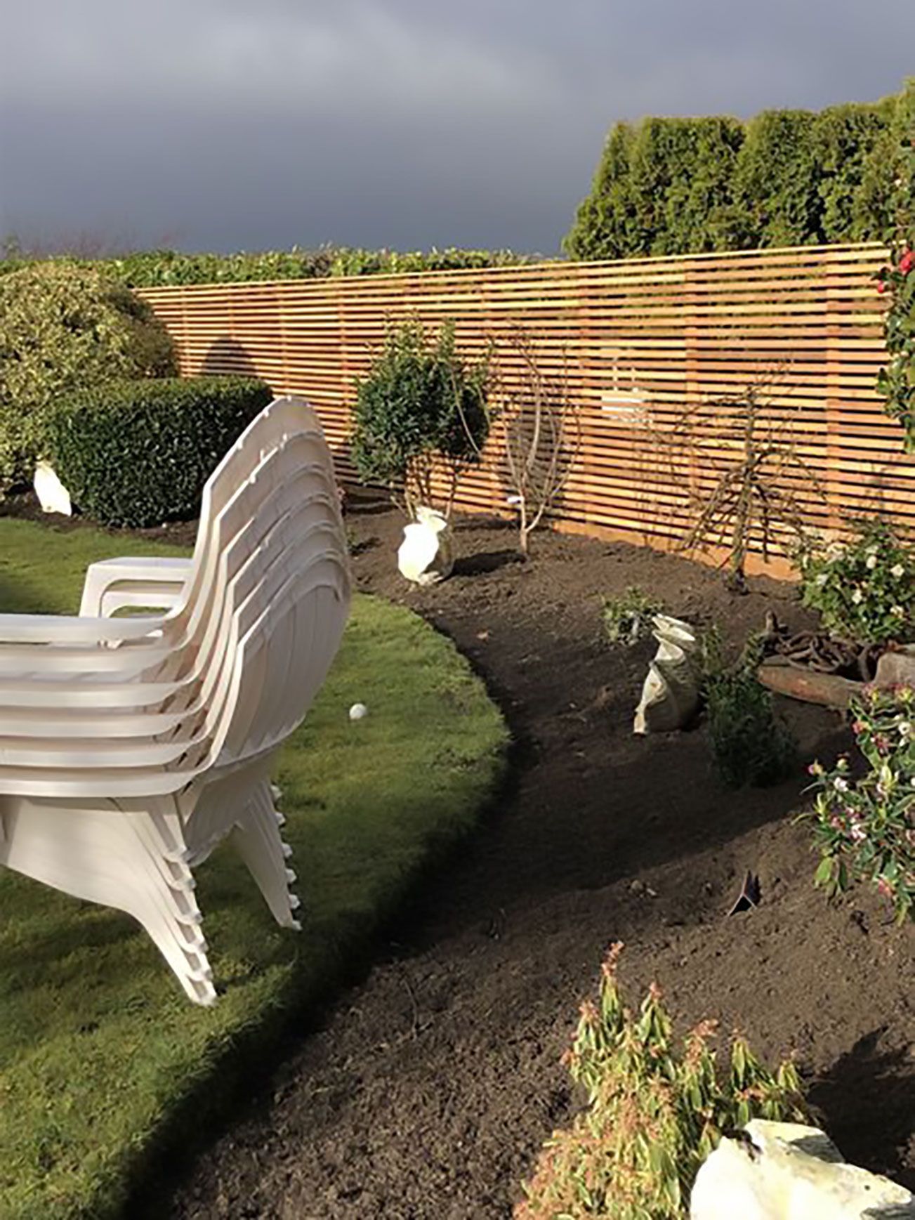 A row of white chairs are stacked on top of each other in a garden.
