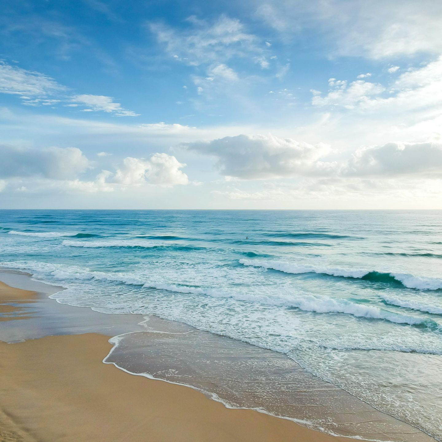 Sandy beach with gentle ocean waves under a partly cloudy blue sky