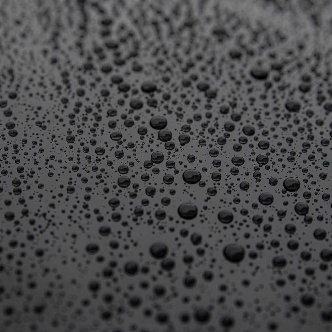 Water droplets on a dark, reflective surface, creating a textured pattern.