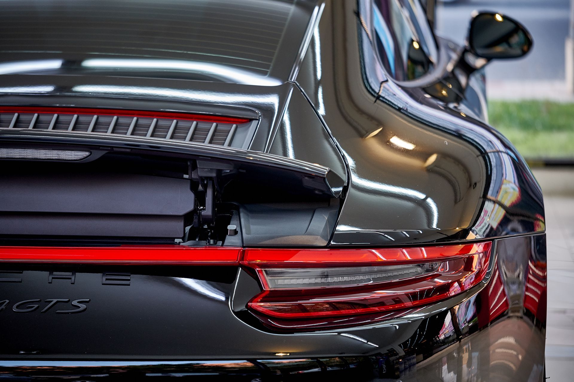 Black Porsche 911 GTS rear detail with red taillights and spoiler. Shiny surface, indoor setting.