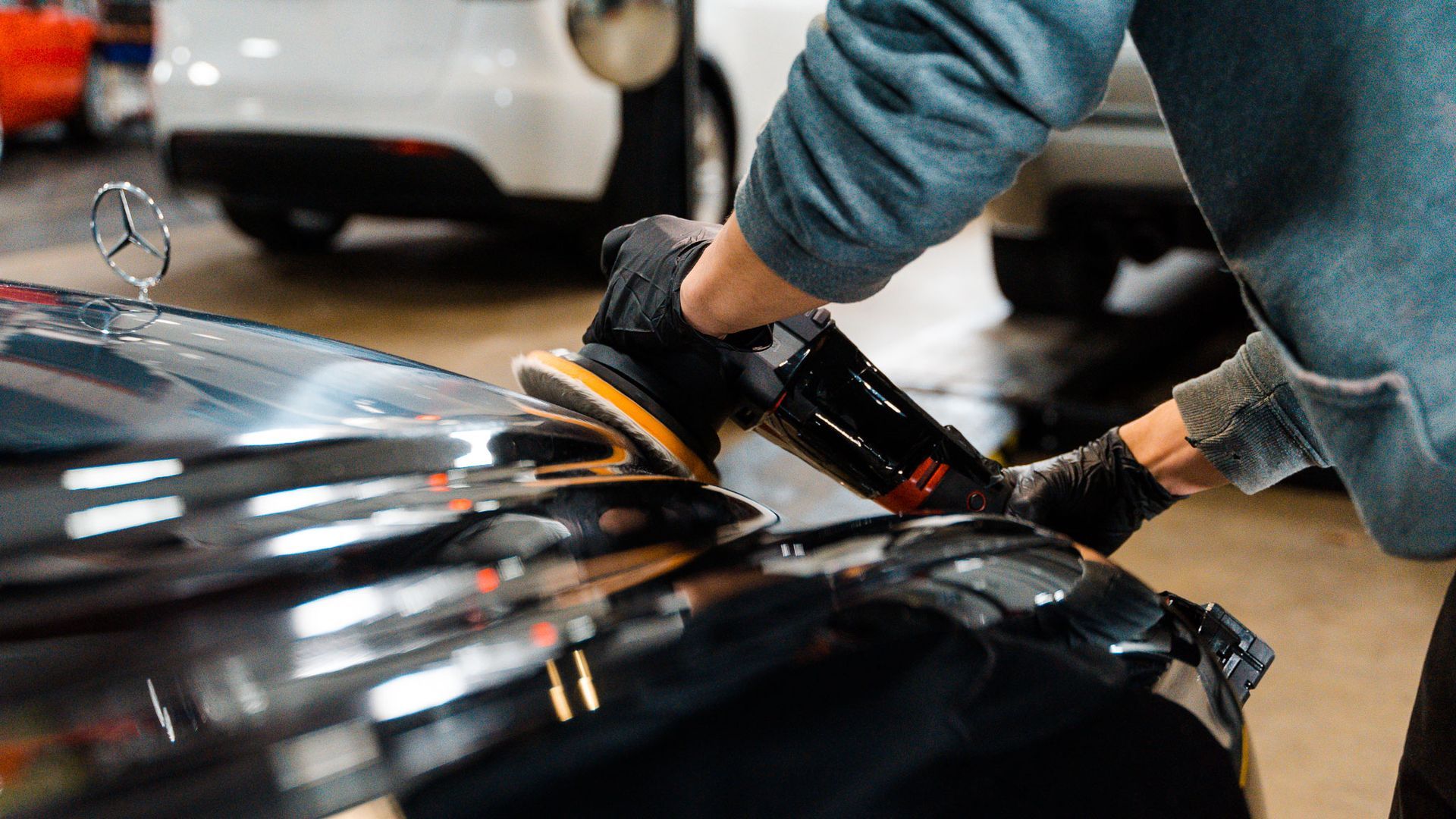 Person using a polisher on a black car's hood, likely detailing.