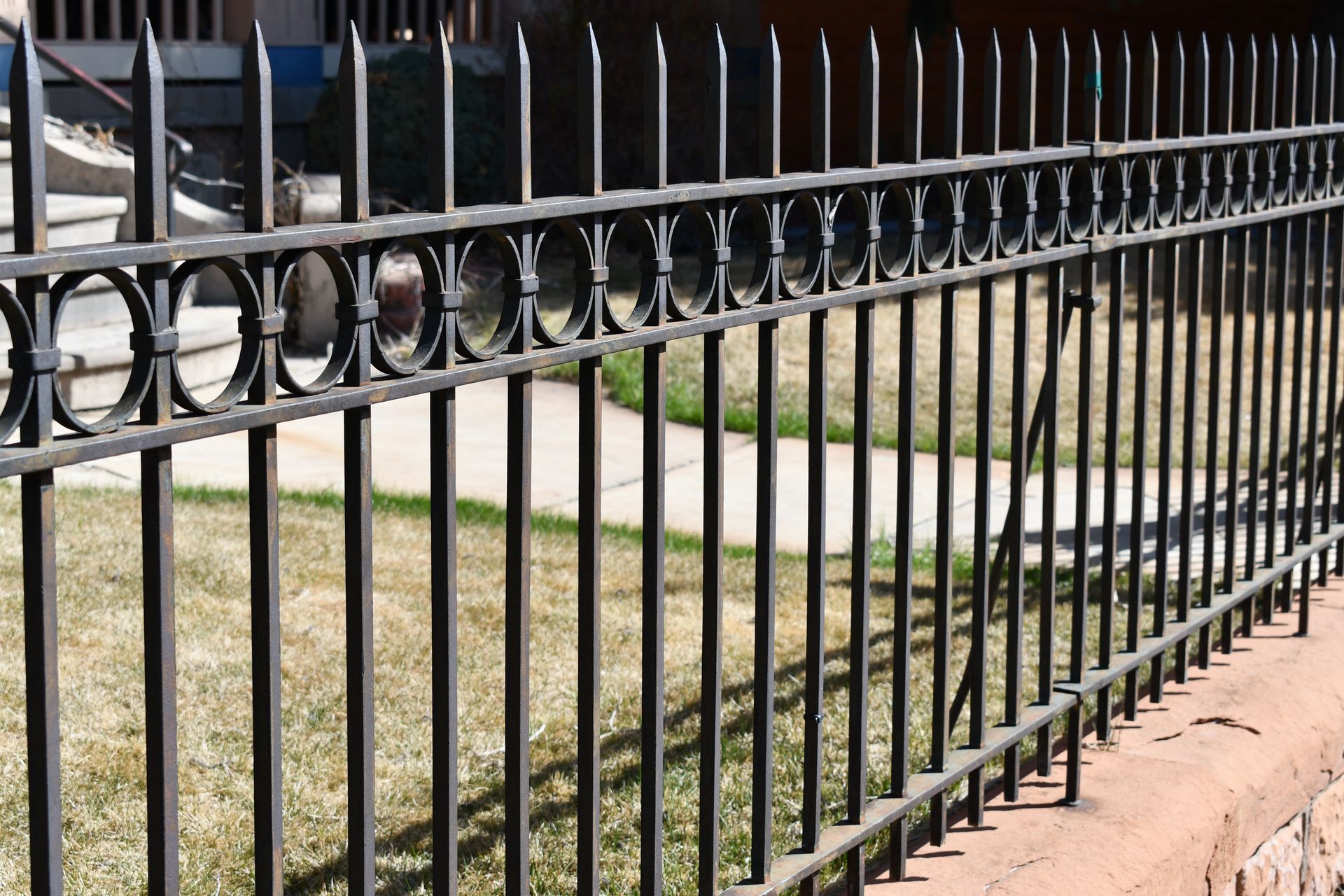 Black iron fence along a sidewalk beside a grassy yard and stone wall
