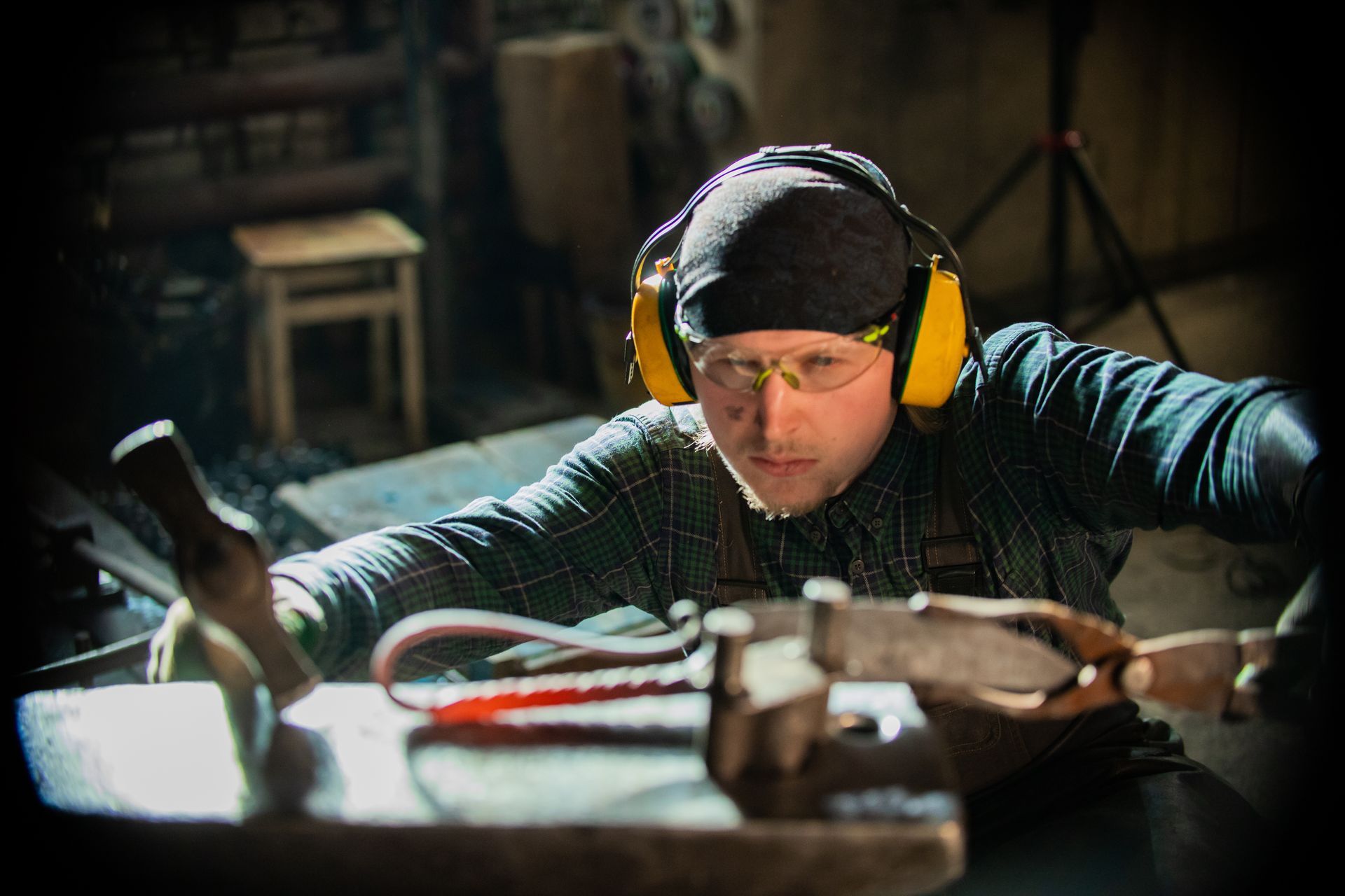 A blacksmith in protective glasses and holding a hammer is making a functional ironwork design. A blacksmith in protective glasses and holding a hammer is making a functional ironwork design.