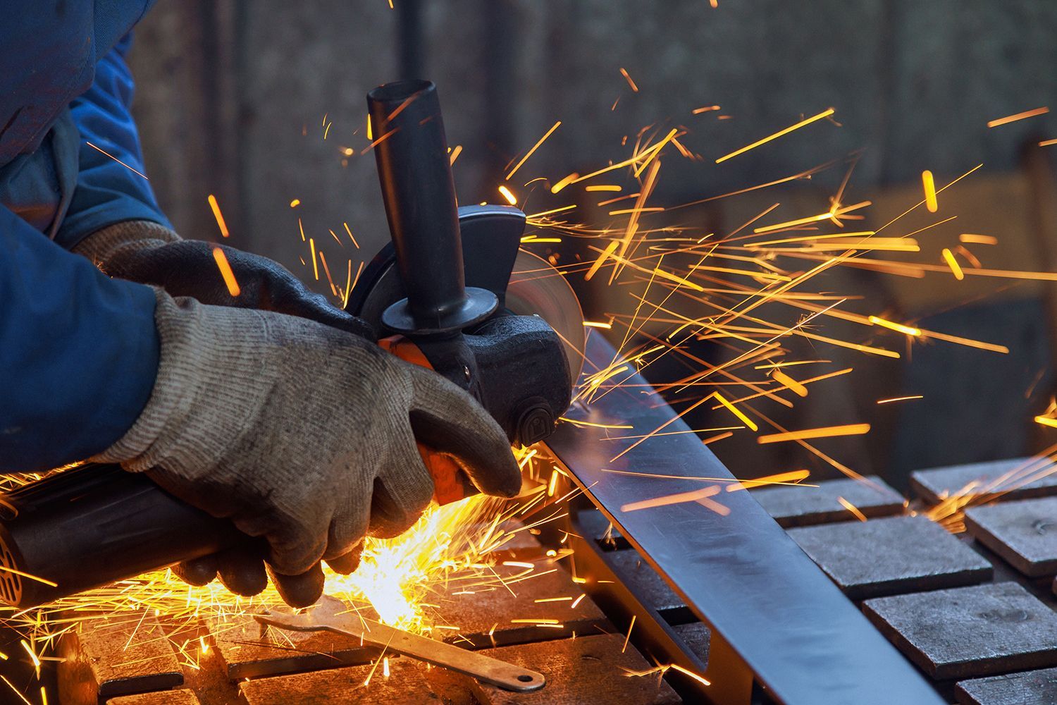 As master metal worker grinds metal on grinder there is spark in factory he works metalwork place.