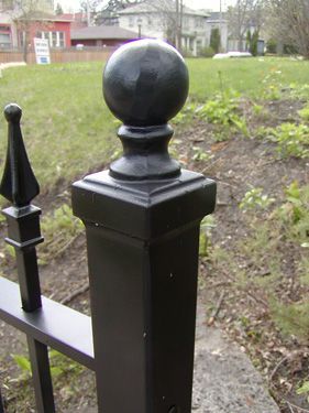 A close up of a black fence post with a ball on top of it.