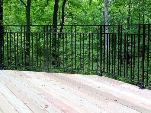 A wooden deck with a metal railing and trees in the background.