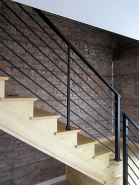 A wooden staircase with a black railing in front of a brick wall