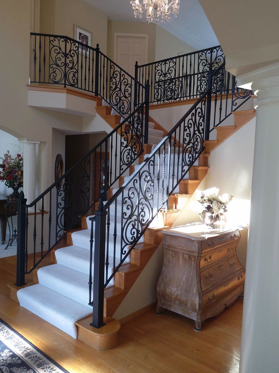 A staircase with a wrought iron railing and white carpet