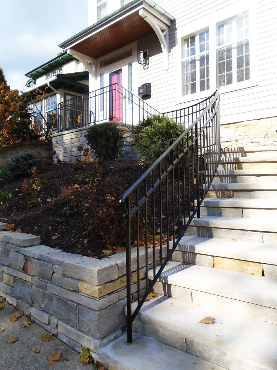 Exterior view of a house with stone steps and black railing leading to a red door. 
